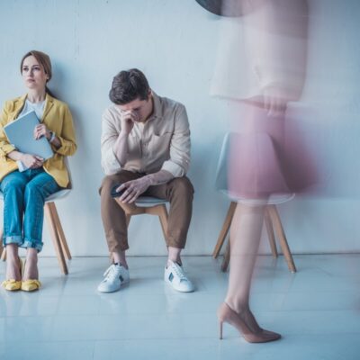 Ludzie siedzący na krzesłach w poczekalni przed sesją terapii współuzależnienia.