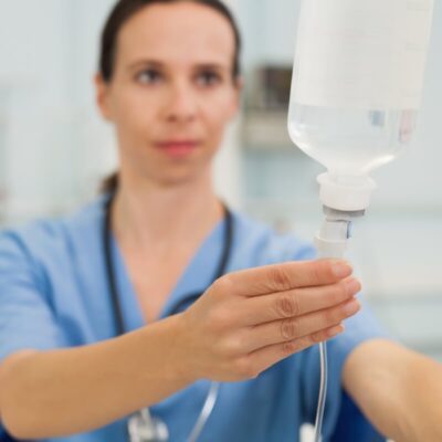 Kobieta w mundurku medycznym przygotowuje kroplówkę, co sugeruje zastosowanie wlewów witaminowych.